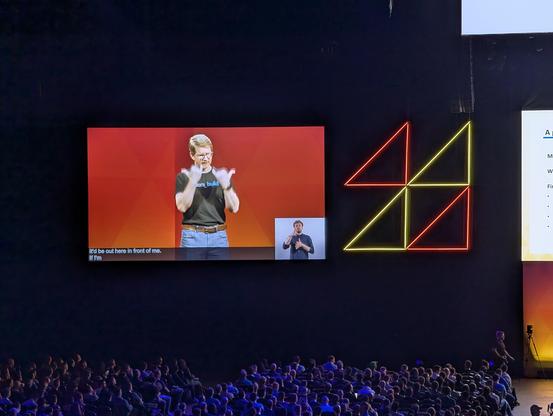 Image of a monitor, showing the speaker signing in ASL, with closed captions and BSL "translation"