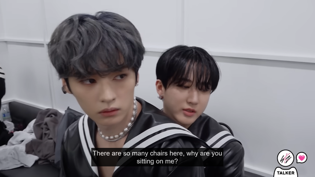 Lee Know pouts slightly as he sits on Changbin's lap. Caption: "There are so many chairs here, why are you sitting on me?"