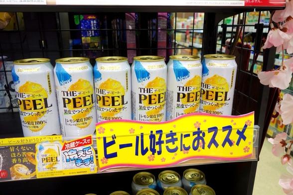 Cans of "THE PEEL" beverage by Suntory, featuring lemon flavor, displayed on a shelf with a bright promotional sign suggesting it's recommended for beer lovers.