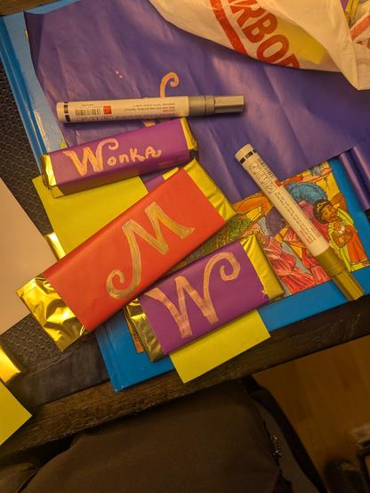 Candy bars wrapped in pink and purple wrapping paper, gold base wrapping,  with gold w's on them to represent 'wonka' bars.