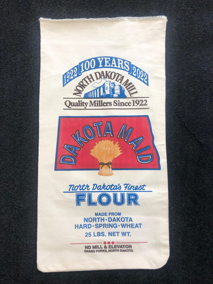 From the North Dakota State Mill's website, a replica cotton flour sack for Dakota Maid, North Dakota's Finest Flour.

Made from North Dakota Hard Spring Wheat.

1922 • 100 YEARS • 2022

A golden sheaf of wheat is pictured atop a reddish-orange silhouette of the State of North Dakota.