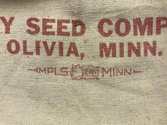 Detail of a burlap seed bag from a company in Olivia, Minnesota. The logo is for Bemis, Minneapolis, Minnesota, and features a cat emerging from the bag.