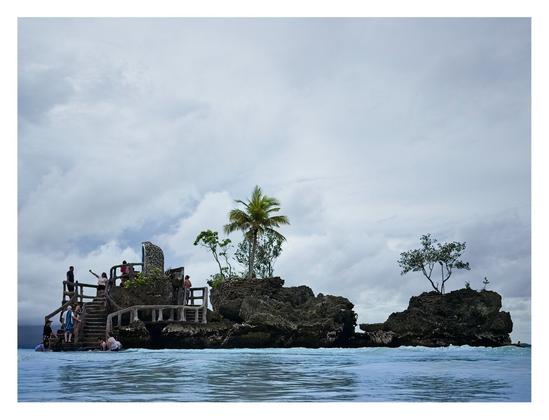 A small Catholic shrine in a rock formation along the ocean water's edge.