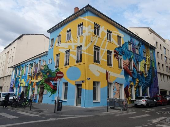 Photo d'un bâtiment pris face à son angle. Sur ses deux façades une grande fresque colorée avec un dragon et un poisson à gauche et un grand poisson à droite. Au centre sur l'angle il y a un cercle jaune avec ce qui ressemble à des idéogrammes chinois ou japonais.