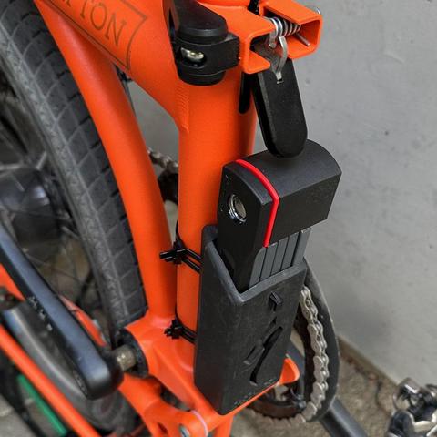 dasselbe Faltrad, aber dieses Mal ist der Hinterbau eingefaltet. Das Fahrradschloss liegt nun frei. Es muss nur die Klinke gedrückt werden und es kann aus seiner Halterung gezogen werden.