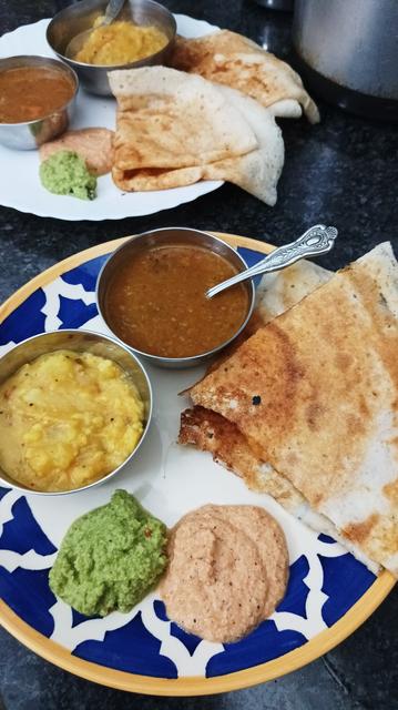 A ceramic plate with dosai, tomato coconut chutney, green coconut chutney, potato bhaji and sambar.
