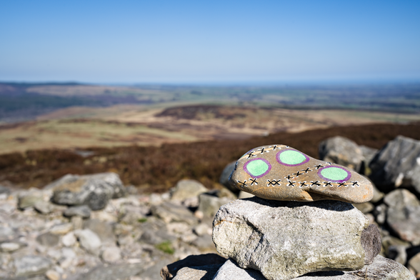 A river or sea pebble, painted with green dots and a stitching effect.