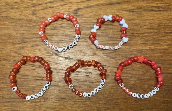Five red kandi bracelets. They all have letter beads that say "#RedInstead" on them. Each one is made out of slightly different shapes and sizes of beads.
