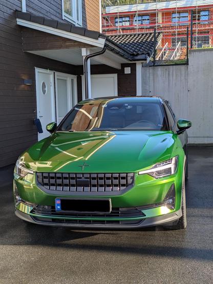 Eit bilde av ein grønn Polestar 2 (elbil) foran inngangspartiet til ei brun leiligheit.
