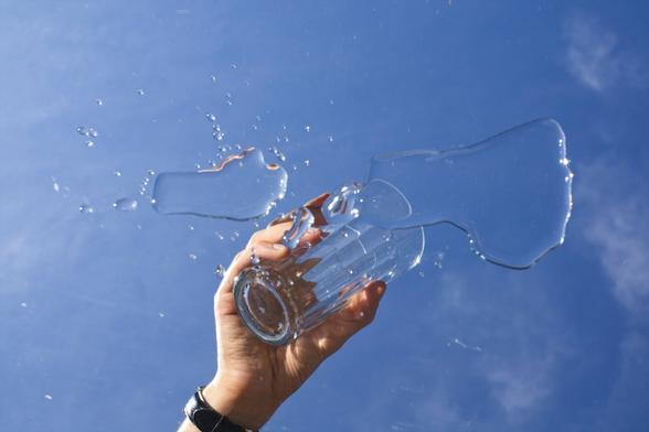 Glass held up by a hand with water in front. Sky with light clouds in the background.