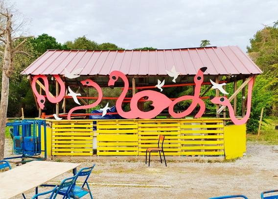La même cabane que la photo d’avant, le bas a été repeint en jaune, sur le haut ont été rajouté des éléments de deco en contre plaqué qui représentent des grands flamants roses de plus de 2 mètres au milieu desquels sont positionnés des petites mouettes en co aussi.