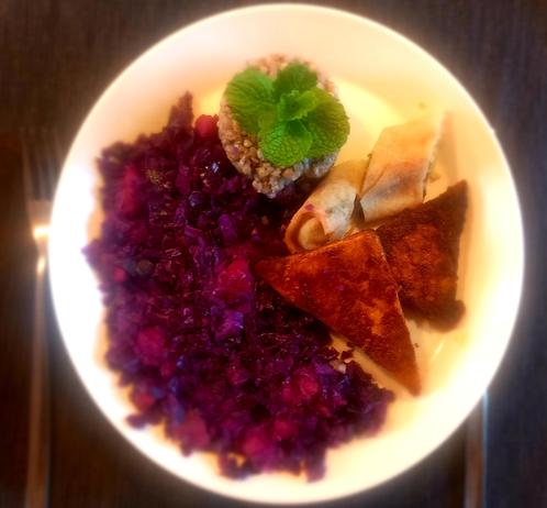 A plate of #vegan food featuring two triangular pieces of fried tofu, a portion of buckwheat garnished with fresh mint, a serving of red cabbage cooked with apple, and two small vegetable spring rolls.