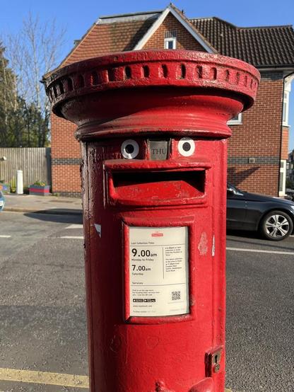A bright red pillar box on a lovely spring day. It has been decorated with googly eyes so that those, the next pickup date label, and the letter slot make a daft smiley face. Googly eyes make EVERYTHING better. Everything. Even googly eyes should have googly eyes stuck on them, and so on ad infinitum.