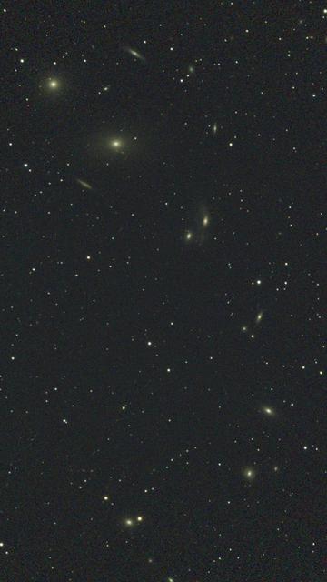A portrait image of Markarian's Chain, a string of galaxies arcing around in a hook from the upper left to the bottom right and back across to the middle.