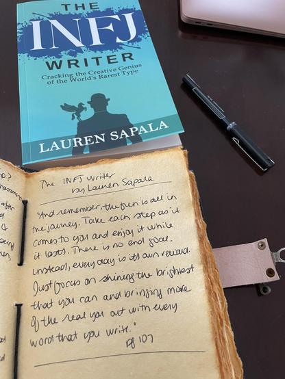 A paperback copy of a book titled "The INFJ Writer: Cracking the Creating Genius of the World's Rarest Type", by Lauren Sapala. The book is placed on a table above a leather-bound journal, where a quote is written.

The quote reads as follows:

"And remember, the fun is all in the journey. Take each step as it comes to you and enjoy it while it lasts. There is no end goal. Instead, every day is its own reward. Just focus on shining the brightest that you can and bringing more of the real you out with every word that you write." –pg 107