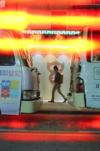 Man quickly walking between two parked mini busses. Glare across the image.