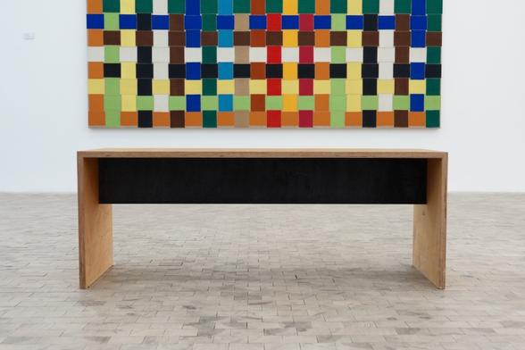 A wooden bench in a gallery, part of a painting in the upper half