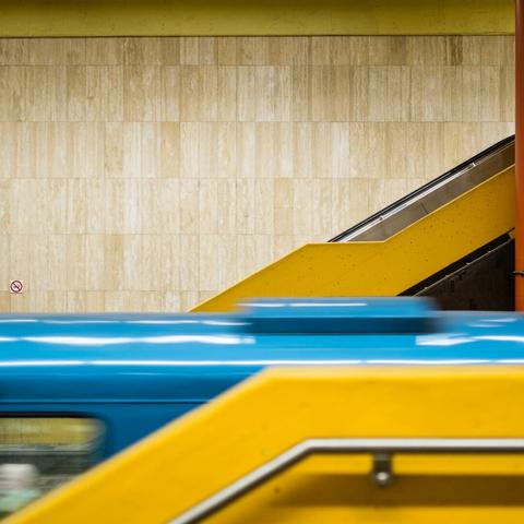Yellow line in diagonal formed by the yellow stairway of a substation, interrupted by the blue horizontal of the subway train moving through.

The tiled yellow-beige wall serve as a background with a lonely no smoking sign on the left breaking the quasi uniform tint.