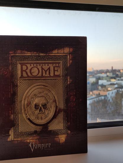 A hardcover book in front of a cuty skyline. The cover is designed like a mosaic covered mostly in blood, with a vampire skull in the center