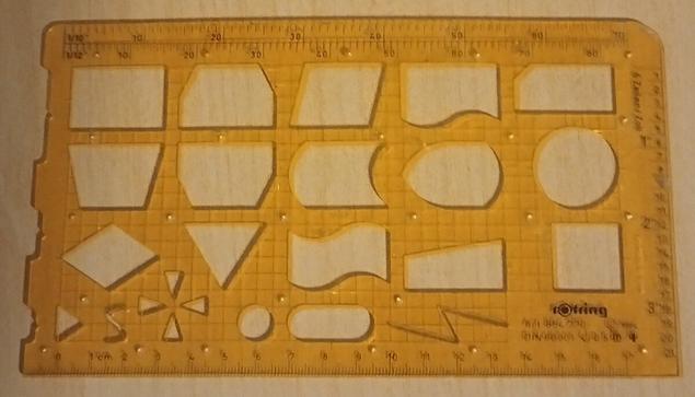 A translucent yellow plastic ruler/stencil with measurements on the edges, and programming flowchart symbols and other diagram features in the middle.
