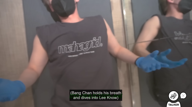 View from above of Lee Know, masked, gloved, and wearing a sleeveless shirt, lying on his back during a workout
