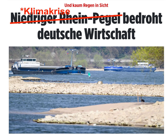 Eine bearbeitete Nachrichtenschlagzeile mit einem Bild von Schiffen auf einem flachen Fluss. Die ursprüngliche Überschrift lautete „Niedriger Rhein-Pegel bedroht deutsche Wirtschaft“, wobei „Niedriger Rhein-Pegel“ durchgestrichen und durch „Klimakrise“ ersetzt wurde. Darüber steht in kleiner roter Schrift: „Und kaum Regen in Sicht“. Im Hintergrund sieht man einen niedrigen Wasserstand mit Sandbänken, die aus dem Fluss ragen.