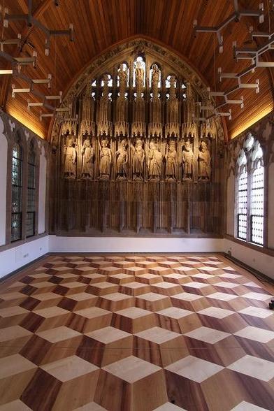 Historisches Rathaus, Hansasaal, Foto: Stadt Koeln, Stadtkonservator, Dorothea Heiermann auf https;//www.museenkoeln.de
Zeigt die rautenförmig sich wiederholende Parketgestaltung des Raumes mit einer scheinbar vertikalen Tiefenwirkung im Dreidimensionalen, der Holztäfelung mit Holzstatuen an der Stinwand, einem gotischen Fenster der Fensterreihe auf der rechten Seite nach außen und auf der linken Seite zum Gebäudeinneren gerichtet.