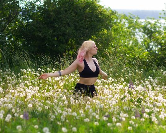 A woman in sports bra enjoying sunshine on a dandelion meadow