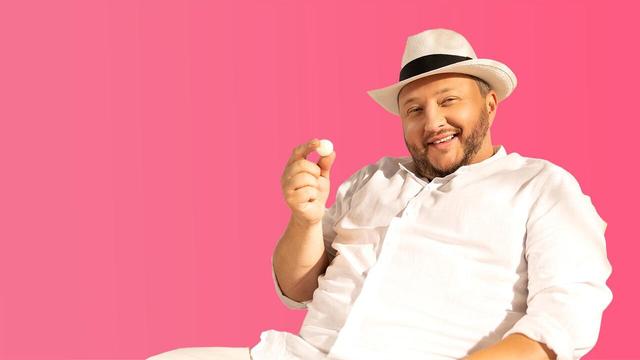 Sebastian Lege sitzt vor einem rosa Hintergrund und hält ein Ferrero Raffaello mit der rechten Hand hoch.