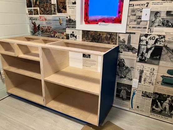 Cabinets for the kitchen in place against a wall covered in pages from old magazines.