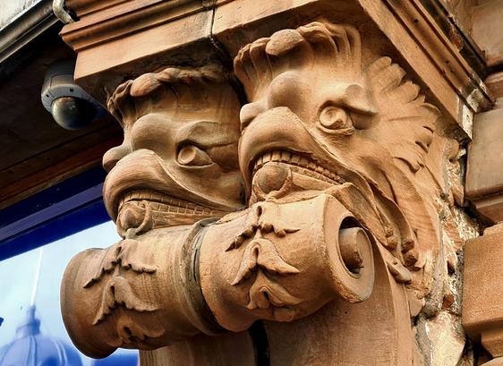 The heads of two griffin-like creatures on the corbles of a former Victorian Bank building.