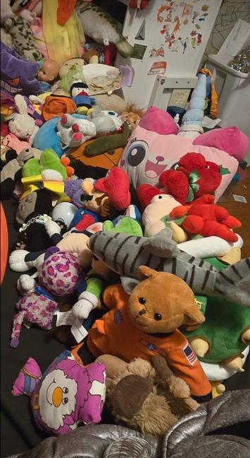 Tight crop showing 1/2 of a twin size bed with black sheets and full of stuffed animals.