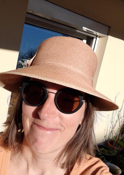 Sabine mit Sonnenhut, getönter Brille und Sonne im Gesicht, lächelnd