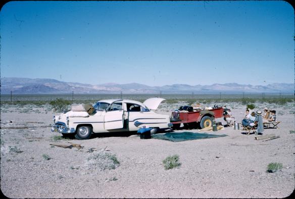 1952 Death Valley Trip, a car with doors and trunk open and a trailer attached, people sitting on folding chairs in a desolate setting