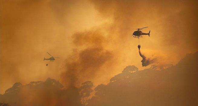Fire-fighting helicopters drop water onto a wildfire.