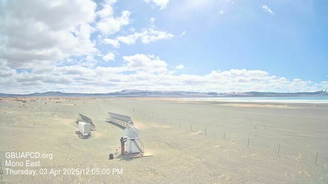 A small figure can be seen working on some infrastructure near Mono Lake. It’s a bright day despite the clouds that appear on the left. The lake is barely discernible in the distance on the right. A fence cuts diagonally through the image.
