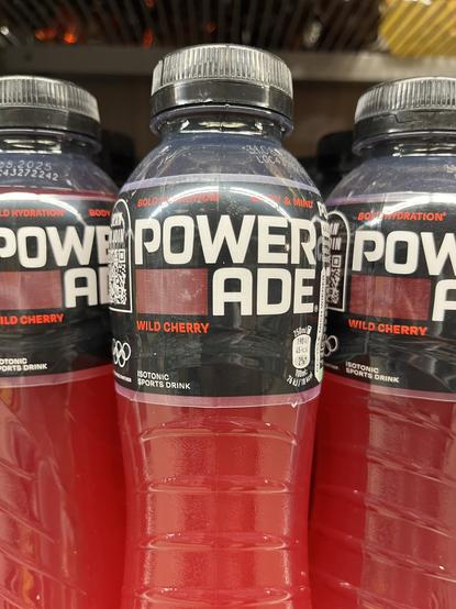 Flaschen mit einem roten Inhalt. Auf dem Etikett steht „Powerade“, aber ein Zeilenumbruch macht daraus „Power ade“