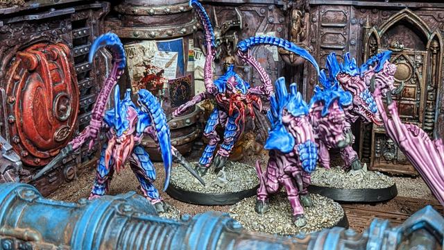 A group of Tyranids aliens painted in blue and purple. Here you can see parts of the group and posters in the background. And a red hatch on the left.