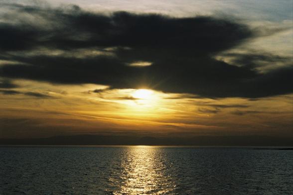 A photo of a sunset over the sea, dark clouds are partially obscuring the setting sun