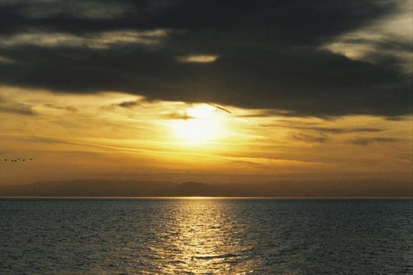 A photo of a sunset over the sea, dark clouds are partially obscuring the setting sun