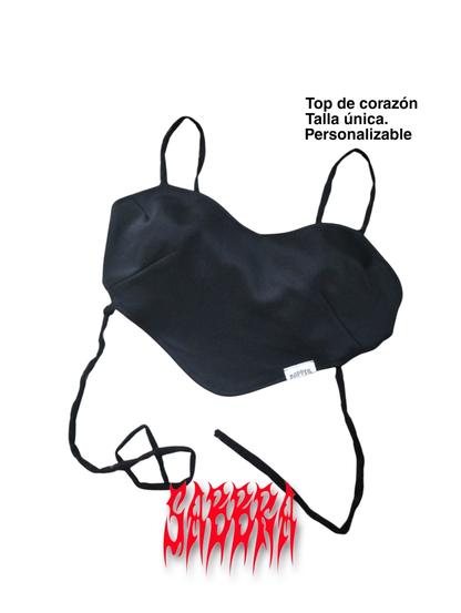 Un top negro en forma de corazón se muestra sobre un fondo blanco. El top tiene tirantes finos y está hecho de una tela que parece suave. Las tiras están atadas en un nudo simple debajo del top. Debajo del top, hay un logotipo o marca en rojo con un estilo de fuente gótica roja que dice "sabbra"