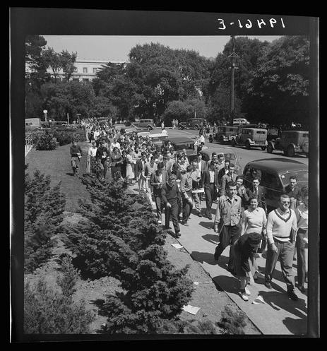 A black and white photograph depicting a large crowd, possibly of students or military personnel walking down a street lined with trees. The photo seems to have been taken on March 1st, judging by the date noted in the upper left corner. It features several individuals wearing various types of uniforms, suggesting some sort of organized gathering or march.