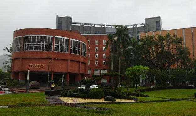 One particular building on the campus of Academia sinica, in red brick with a rotunda building, and with a lush green landscape around, including some palm trees.