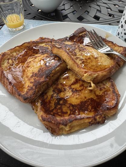 Some absolutely fabulous french toast The Man made this past weekend out of brioche bread.  The best I've ever had anywhere.

Yes, yes, it is a lot of maple syrup.  Jeez, you guys never give up.

Three (yes THREE) slices of french toast are slathered, drowning in maple syrup on a white plate.  A fork sits on top of them, and NO ONE has had any of it yet.  This is a bleeding miracle.

Some orange juice remains in a small glass to the left, the bottom of a coffee cup is visible to the right.  The blue placemat is on a metal trellis outdoor-style table because it is finally warm enough for us to be out in the sunroom again.  Yay.