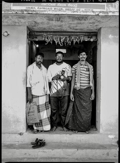 3 men stand in a doorway, the one in the center is holding a camera.