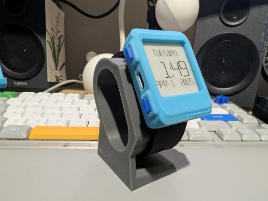 Watchy eink watch with a blue 3d printed case and affixed to a grey watch stand