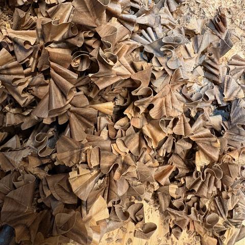 The image presents a close-up view of a pile of walnut wood shavings, showcasing their intricate details and textures. The wood shavings are brown in color and have a rough, irregular shape.