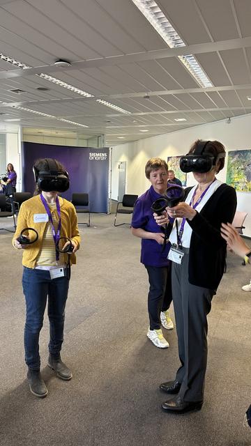Staatssekretärin Dr. Ute Leidig und ein Mädchen testen beim Girls'Day bei Siemens Energy Global GmbH & Co. KG. den Umgang mit Virtual Reality (VR). Beide tragen VR-Brillen und halten Steuergeräte in den Händen. Unterstützt werden sie durch eine Mitarbeiterin des Unternehmens.