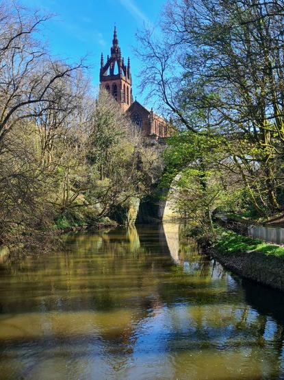 A red sandstone church and an arched bridge rising high above a tree-lined river.