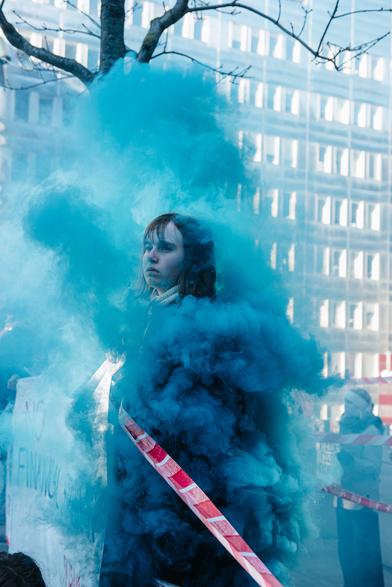 A girl holding corner of a banner and the blue smoke is circling around her like a magic spell from a movie scene.